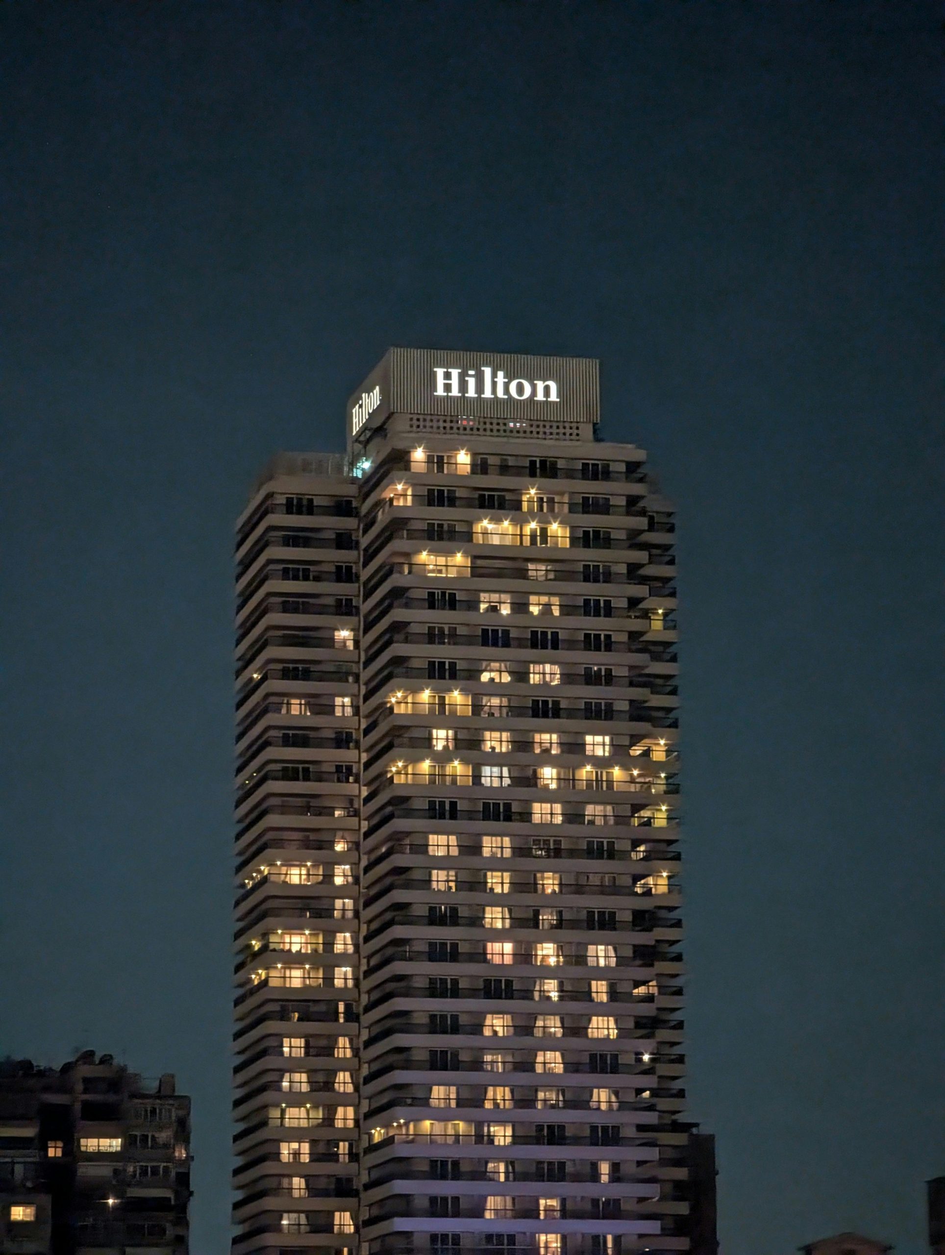 High-rise Hilton hotel building, illuminated at night against a clear sky. Ideal for cityscape and travel themes.