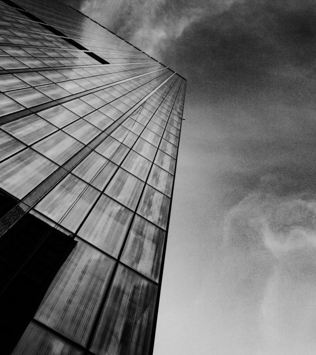 Low angle shot of a modern skyscraper with dramatic black and white tones, emphasizing architectural lines.